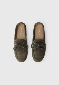Dark olive green suede boat shoes with a rounded toe, lace-up design, and contrast stitching, featuring a textured insole with brand logo.