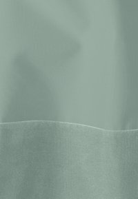 Tissu vert clair avec une texture lisse, présentant une bande horizontale contrastante d'un vert légèrement plus foncé au bas.