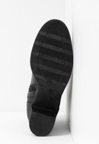 Suela de zapato negra con un diseño liso, líneas texturizadas para agarre y un tamaño marcado "37". El ángulo muestra un ligero tacón.