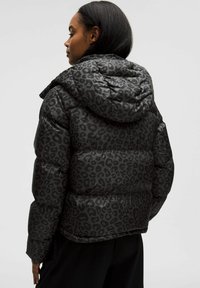 Jachetă neagră căptușită cu glugă, având un model texturat de leopard închis, design matlasat și manșete ribbate. Vedere din spate.