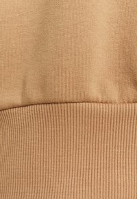 Tessuto di cotone marrone chiaro con una superficie liscia e una texture a coste nella parte inferiore. Nessun motivo visibile o dettagli hardware.