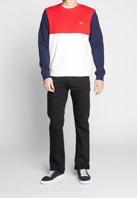 Bluza w kolorowe bloki, posiadająca czerwony górny element, biały środek i granatowe rękawy. Połączona z czarnymi spodniami i granatowymi butami.