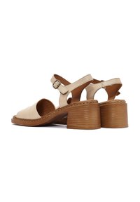 Sandali in pelle beige con punta aperta, cinturino alla caviglia e tacco a piattaforma in legno. Presentano lati intagliati e dettagli di cucitura lungo la suola.