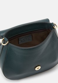 Petit sac à main en cuir teal avec un fermoir à pression doré, présentant une finition texturée et un intérieur spacieux de couleur marron.