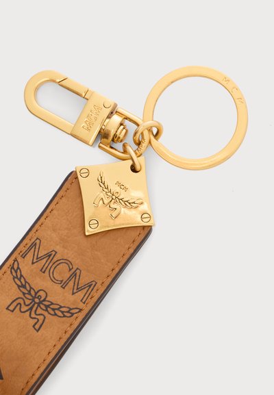 Porte-clés et attache en métal doré fixés à une lanière en cuir marron avec logo MCM noir et motif laurier.