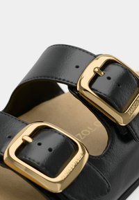 Μαύρη δερμάτινη σαγιονάρα με δύο ρυθμιζόμενες λωρίδες και χρυσές αγκράφες, υφασμάτινη επιφάνεια και μπεζ εσωτερική σόλα.