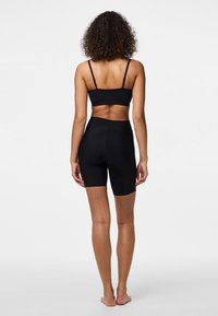 Bralette nera attillata e pantaloni shorts a vita alta, realizzati in tessuto morbido, con spalline regolabili e design senza cuciture.