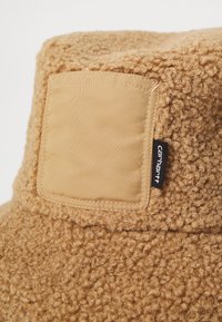 Col en polaire beige au fini bouclé, avec des détails cousus et un patch en tissu lisse contrastant. Inclut une étiquette de logo noire.