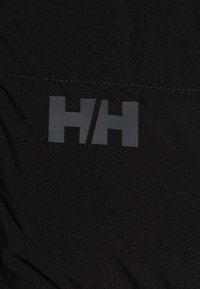 Juodas audinys su dideliu pilku, stilizuotu "H/H" logotipu. Lygi tekstūra su matomomis siūlėmis palei siūlę.