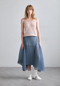 Top senza maniche rosa con paillettes, abbinato a una gonna plissettata blu fluente. Modella che indossa sneakers bianche con dettagli argentati.