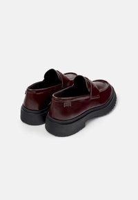 Burgundy nahkakengät, joissa on sileä pinta, musta kumipohja, mokka-malli sekä merkkilappu kantapäässä.
