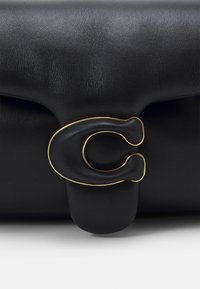 Czarna skórzana torebka z charakterystycznym zapięciem w kształcie litery C z złotym wykończeniem oraz teksturowaną powierzchnią.