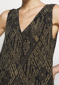 Ärmlös topp i svart och olivgrön med intrikata geometriska och tribalmönster, med en V-ringning.