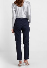 Marineblau gestreifte Hose aus glattem Stoff, mit hoher Taille und schlanker Passform, kombiniert mit einem metallischen Langarmoberteil und transparenten Absätzen.