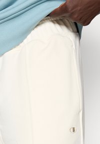 Ανοιχτόχρωμο κρεμ παντελόνι φόρμας με ελαστική μέση και τσέπες στο πλάι, με μικρό κεντητό λογότυπο σε αντίθετο χρώμα.