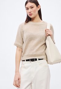 Šviesiai rudas trumpomis rankovėmis megztinis su minkšta tekstūra, derinamas su kreminėmis kelnėmis ir šviesios spalvos peties krepšiu. Juodas diržas suteikia kontrasto.