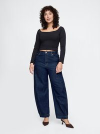Schwarzes Langarm-Crop-Top, kombiniert mit hochgeschnittenen, weiten blauen Jeans und braunen hochhackigen Schuhen, mit einer glatten Textur.