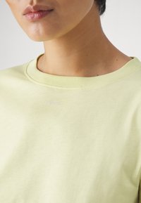 Ljusgul bomulls-t-shirt med rundad halsringning och en liten "PINKO"-logotyp i lavendel på bröstet, mjuk textur och slät finish.