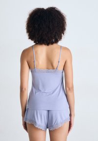 Camisole lilas clair avec dentelle, associée à un short assorti avec des accents en dentelle sur l'ourlet. Tissu doux avec une coupe décontractée.