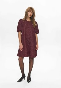 Burgundi puff-sleeves ruha texturált virágmintával, térdig érő, kerek nyakkivágással, fekete, áttetsző harisnyával és hegyes orrú magassarkú cipővel párosítva.