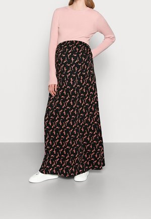 Black maxi skirt with a floral pattern in pink, paired with a fitted pink ribbed long-sleeve top. Model wearing white sneakers.
