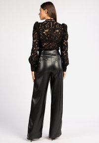 Zwarte kanten langslijf top met bloemenpatroon en pofschouders, gecombineerd met hoge taille zwarte faux leren wijde broek.