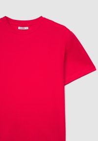 Maglietta a maniche corte con scollo tondo in cotone rosa acceso. Presenta una tessitura liscia e cuciture sottili. Etichetta visibile all'interno dell'area del collo.