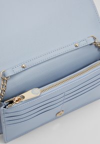 Wnętrze torebki z jasnoniebieskiej, teksturowanej skóry ze złotym zamkiem błyskawicznym i okuciami. Widoczne liczne kieszonki na karty oraz gładka podszewka.
