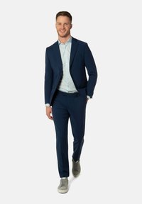 Marineblauer Anzug mit taillierter Passform und glattem Textur, kombiniert mit einem hellblauen Hemd. Tragen Sie dazu graue Sneakers für einen modernen Look.