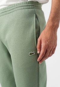Grønne sweats har en ribbet talje, sidelommer og et lille broderet krokodillelogo på venstre lår. Blød tekstur.