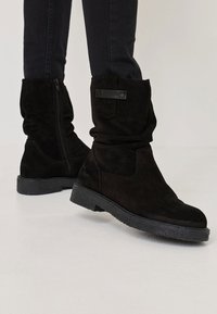 Stivali alla caviglia in suede nero con un design arricciato, cerniera laterale, suola in gomma testurizzata e un pannello decorativo sul retro.