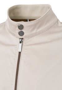 Helle beige Jacke mit Stehkragen, ausgestattet mit zwei Druckknöpfen, einem Frontreißverschluss mit texturiertem Ziehband und Steppnähten.