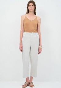 Tan mouwloze top met een V-hals, gecombineerd met hooggesneden lichtgrijze broek en platte sandalen, met een gladde stof en een gepaste pasvorm.