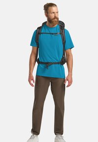Camicia blu a maniche corte, pantaloni marroni e uno zaino nero con tracolle. Presenta fibbie regolabili e tasche sui pantaloni.