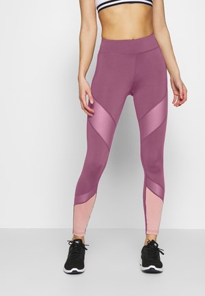 Mauve leggings med mat yta, med kontrasterande glansiga rosa paneler och design med hög midja. Kombineras med svarta träningssneakers.