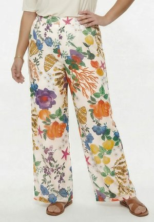 Weit geschnittene weiße Hose mit bunten Blumen- und Korallenriffmustern, getragen mit braunen Sandalen und einem hellbeigen Oberteil.