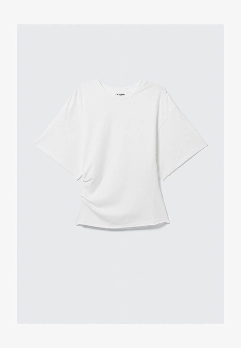 T-shirt bianco oversize a manica corta con scollo rotondo e vestibilità morbida, posizionato piatto su uno sfondo grigio chiaro.