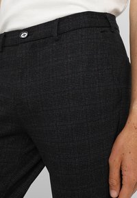Donkergrijze broek met een fijn ruitpatroon en subtiele bordeauxrode lijnen, met een zichtbare knoopsluiting en voorzakken. Soepele textuur.