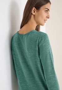 Teal gestrickter Pullover mit weitem Ausschnitt, weichem Material und gerippten Details an den Bündchen und dem Saum. Hat eine lockere Passform und wird von der Seite betrachtet.