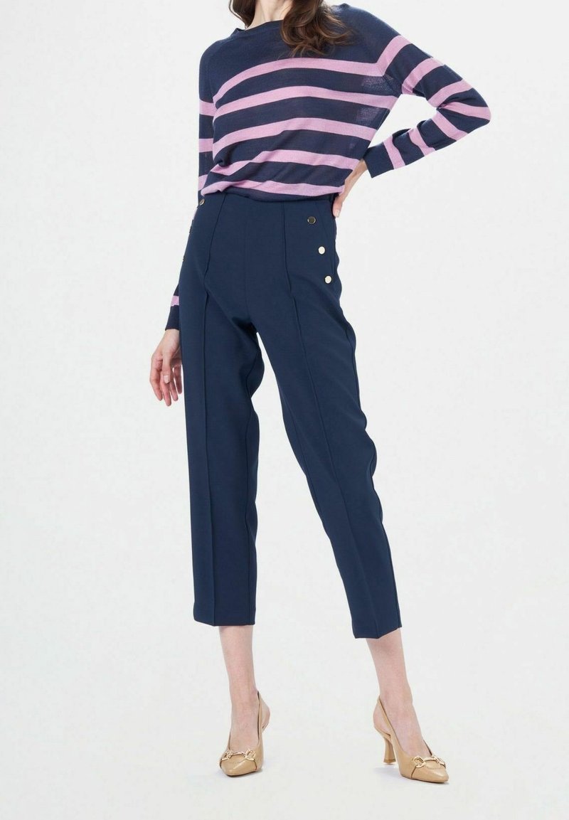 Pantalon marine taille haute avec jambes raccourcies, orné de boutons dorés. Associé à un pull en maille rayé marine et rose.