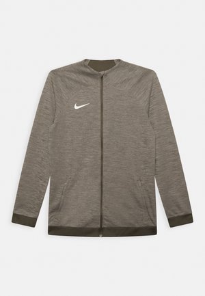 Veste de sport grise avec fermeture éclair à l'avant, col haut et tissu texturé. Présente des accents vert foncé et un logo Nike blanc sur la poitrine.