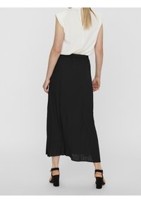 Frau von hinten gesehen, die ein ärmelloses weißes Oberteil, einen schwarzen Midirock und schwarze High-Heels trägt, vor einem schlichten Hintergrund.