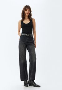Top sin mangas negro acanalado combinado con jeans de piernas anchas de tiro alto y un cinturón negro. La modelo lleva botas negras de tobillo con punta. 
