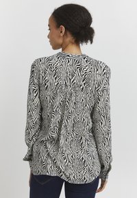 Camicia a maniche lunghe con stampa zebrina bianca e nera, caratterizzata da un design arricciato sulla schiena e sui polsini, realizzata in un tessuto leggero.