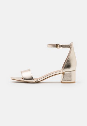 Metalicznie złote sandały na obcasie z paskiem wokół kostki, otwartym noskiem i kwadratowym blokowym obcasem. Gładka faktura i minimalistyczny design.