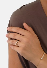 Gold ring and bracelet with clear sparkling stones. Smooth metal finish, floral design with alternating settings. Brown fabric background.
