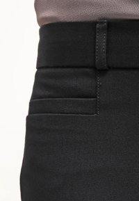 Svarta jeans med en slät textur. Har en figursydd midja och en ficka med subtila horisontella sömmar.