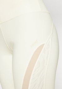 Leggings de color beige claro con un panel de malla transpirable que presenta un sutil patrón de cebra, detalle de logo y una textura de tela suave y elástica.