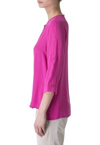 Blouse fuchsia avec des manches trois-quarts, texture lisse, col rond et détail de poignet boutonné. Coupe ajustée, tissu léger.
