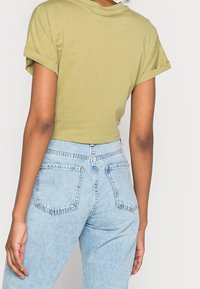 Oliwkowy krótki t-shirt z podwiniętymi rękawami, w zestawie z jasnoniebieskimi dżinsami z wysokim stanem, które mają dwie tylne kieszenie i wyblakłą fakturę denimu.